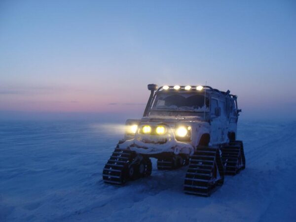 Cape-to-Cape远征的路虎Defender在西伯利亚雪地履带上行驶，车头灯点亮