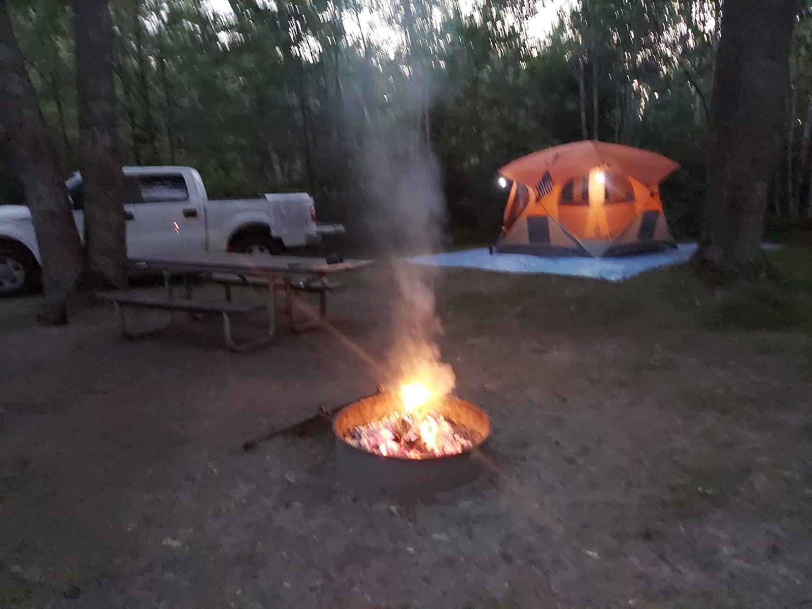 夜晚露营地篝火燃烧，旁有白色皮卡与发光橙色帐篷