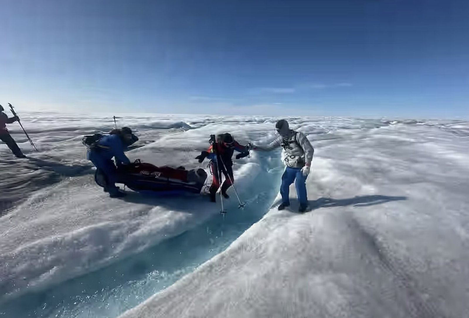 探险队员在蓝色冰裂缝旁合力拖拽红色雪橇