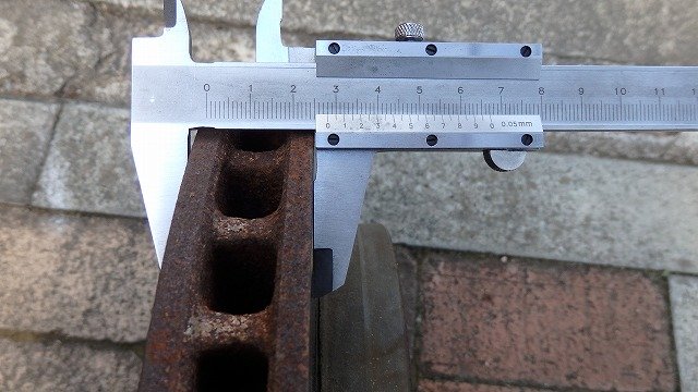 生锈金属件被银色游标卡尺测量于砖石地面