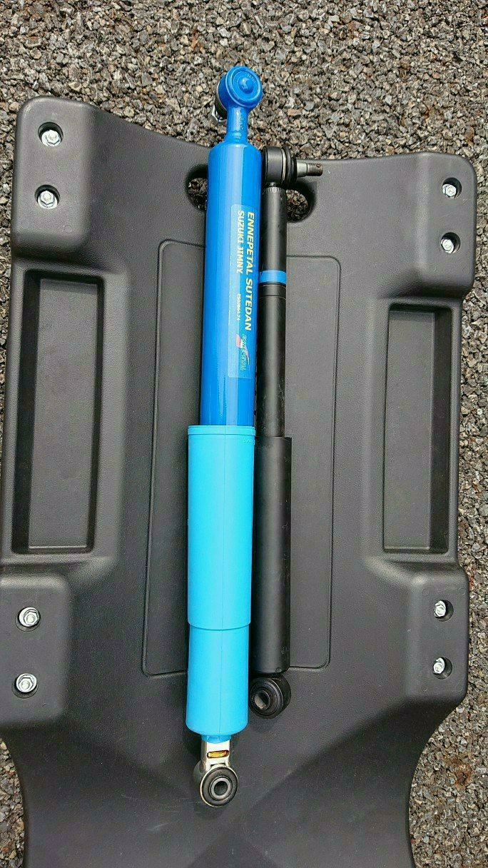 蓝色新转向阻尼器与黑色原车阻尼器置于碎石地面