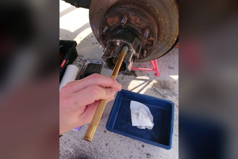 一只手在车库用金色工具拆卸生锈的轮毂