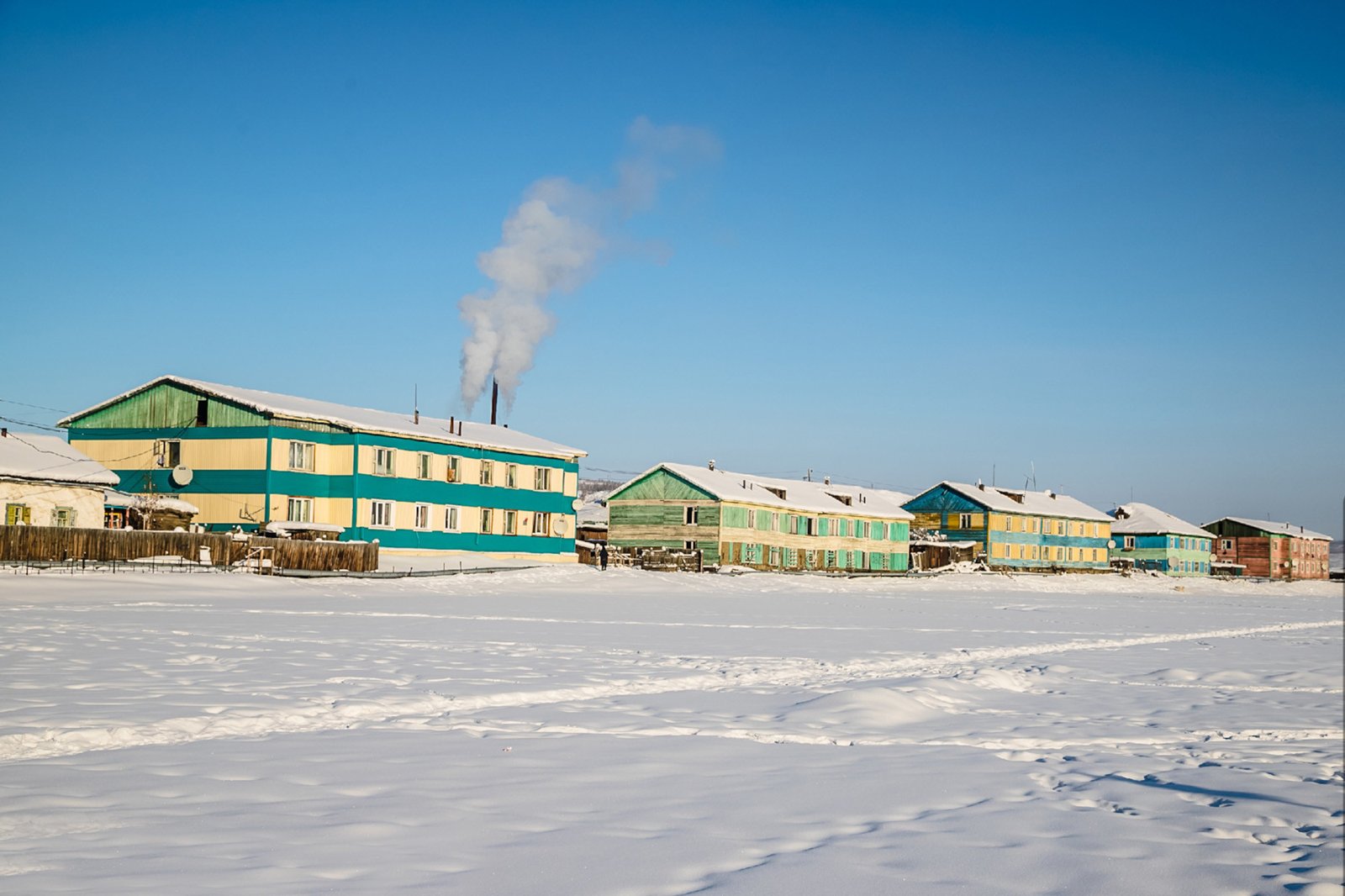 蓝天雪地中一排色彩鲜艳的木屋与升腾的白烟